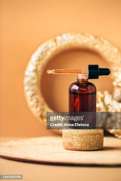 pipette placed on amber glass bottle with essential oil and many air bubbles on cork podium against beige background with gold decorations. concept of natural cosmetic products. front view and close-up - jojoba oil stock pictures, royalty-free photos & images
