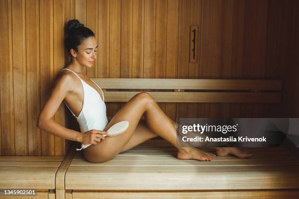 young beautiful multiracial woman making anti cellulite or lymphatic dry massage at  finnish sauna. - natural organic thermo cosmetics foto e immagini stock