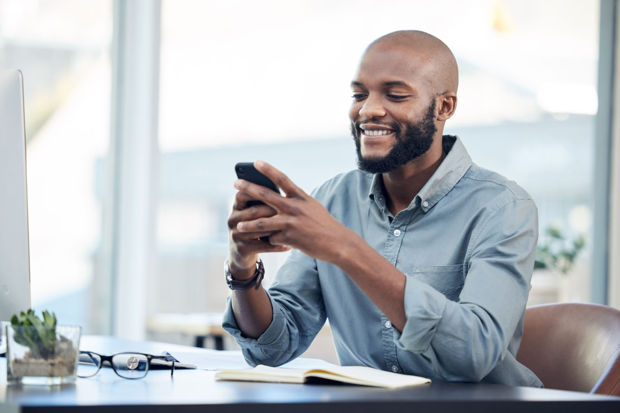Shot of a handsome young businessman sitting alone in his office and using his cellphone Shot of a handsome young businessman sitting alone in his office and using his cellphone