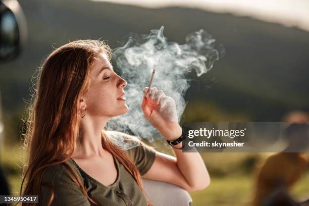 junge rothaarige frau, die in der natur eine zigarette raucht. - woman smoking cigarette stock-fotos und bilder