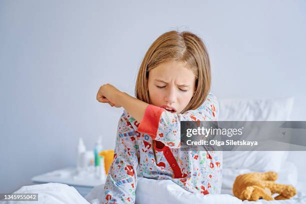 sick child coughs while sitting on the bed - neumonía fotografías e imágenes de stock