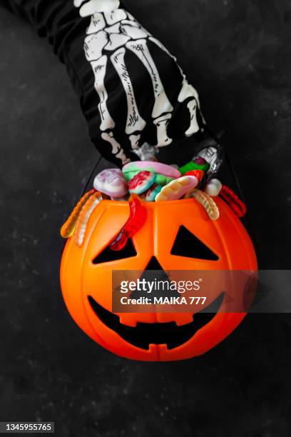 jack o' lantern, trick or treat bucket, filled with candies held by a skeleton hand on black background. halloween celebration concept. - black jack hand ストックフォトと画像