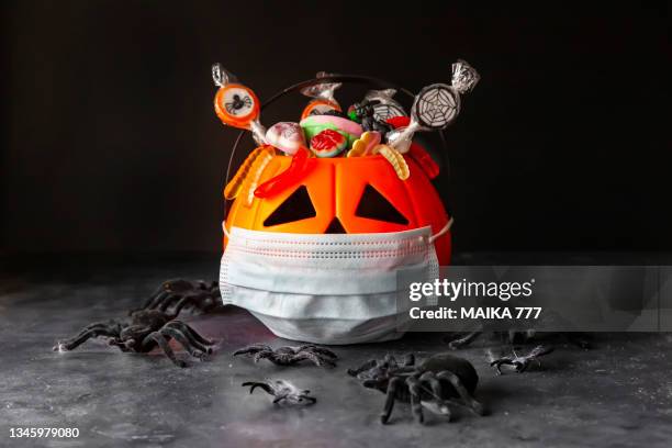 jack o'lantern, trick or treat bucket, filled with candies with protective face mask on black background. halloween celebration  in times of pandemic. - scary pumpkin faces stock pictures, royalty-free photos & images