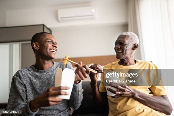 grandson and grandfather talking and eating take out food at home - chinese takeout stock pictures, royalty-free photos & images