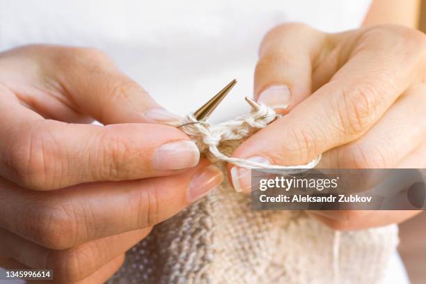 a young woman knits a stylish modern fashion cardigan, jacket or sweater with knitting needles, sitting on a wooden chair or bench in the open air. the concept of a hobby, world knitting day in public. close-up. - knitting needles stock-fotos und bilder