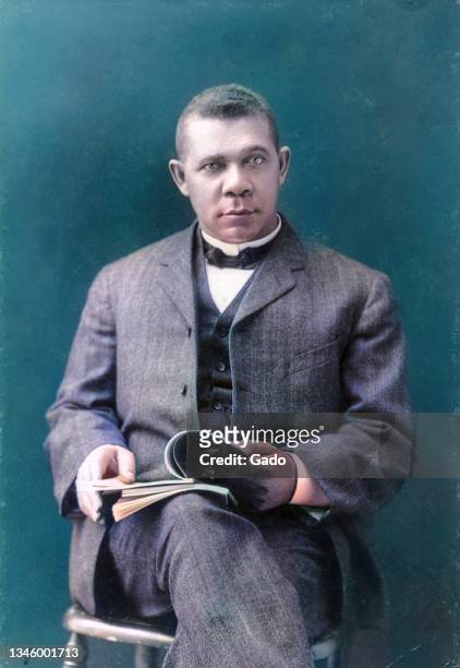 Three quarter length portrait of Civil Rights activist Booker T Washington reading a book and seated on a stool, 1903. Note: Image has been digitally...