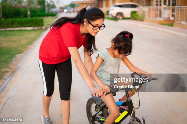 hermana pequeña supervisando a su hermana pequeña aprendiendo bicicleta. - sobrina fotografías e imágenes de stock