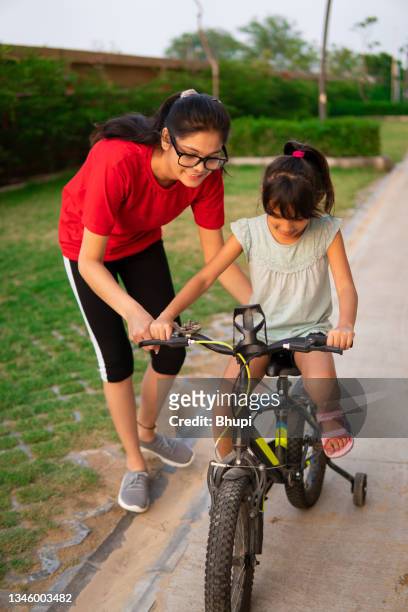 young sister supervising her little sister learning bicycle. - nichtje stockfoto's en -beelden