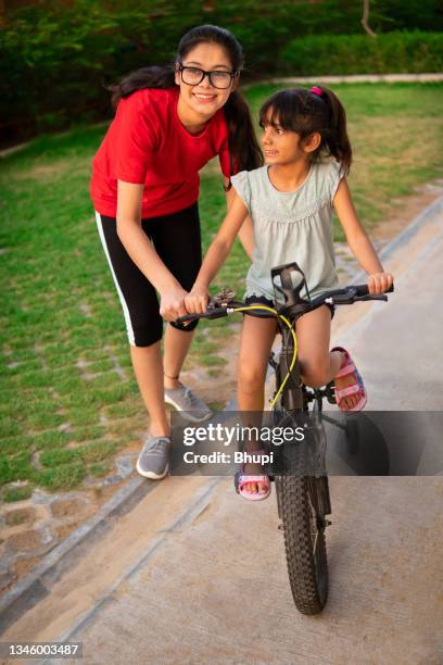 young sister supervising her little sister learning bicycle. - indian aunt stock pictures, royalty-free photos & images