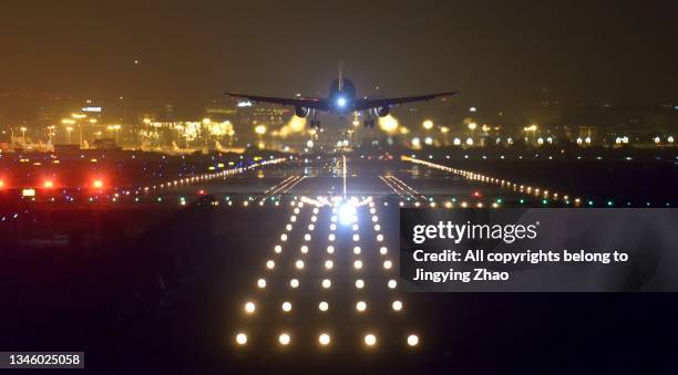 aircraft landing in front of runway lights of airport late at midnight - runway night stock pictures, royalty-free photos & images