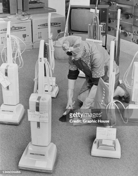 Cleaner sweeps the floor in between a display of new Hoover and Electrolux vacuum cleaners, USA, circa 1965.