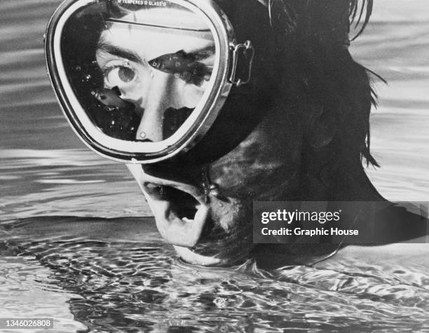 Man wearing a tempered glass swimming mask, with a pair of fish on the inside, USA, circa 1965.