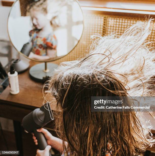 a child blow dries her hair at a vanity table - drying hair stock-fotos und bilder