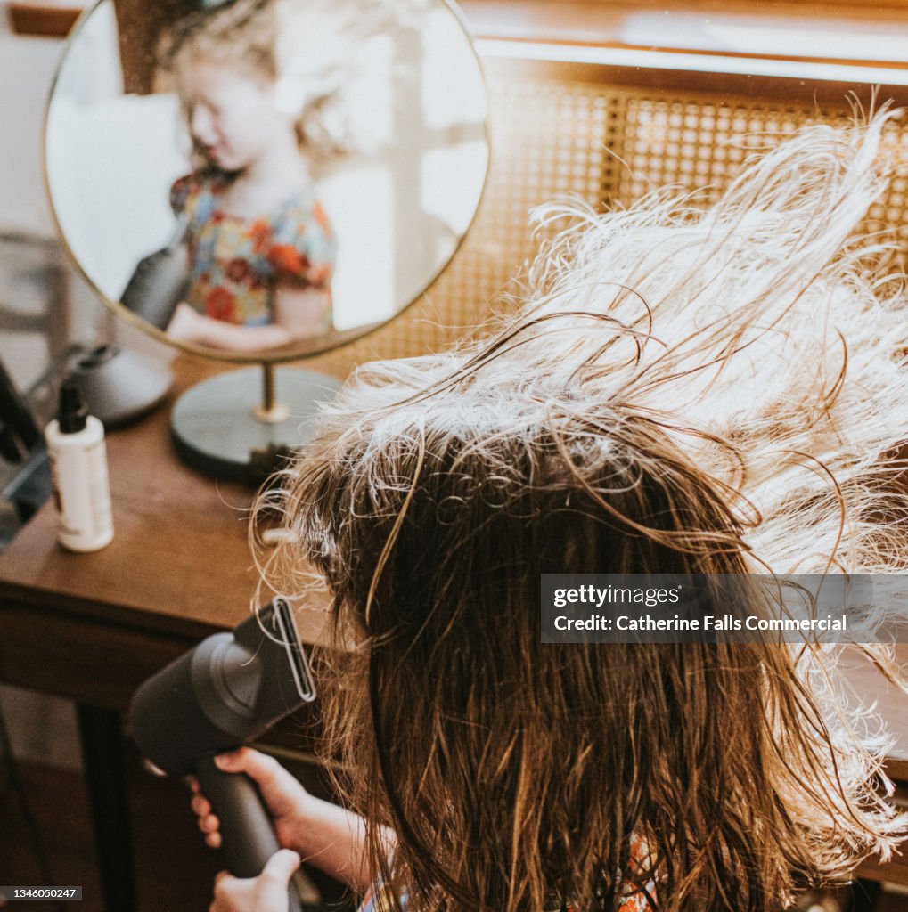 A child blow dries her hair at a vanity table