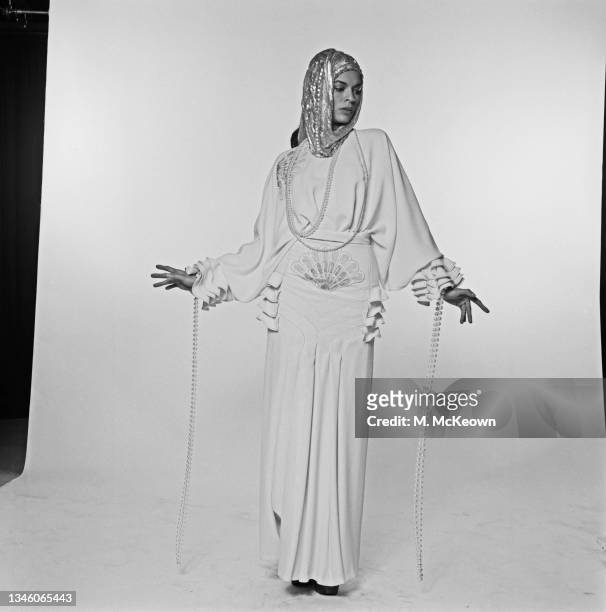 Nicaraguan actress Bianca Jagger, the wife of singer Mick Jagger of the Rolling Stones, modeling an evening dress with long beaded cuffs and a hood,...