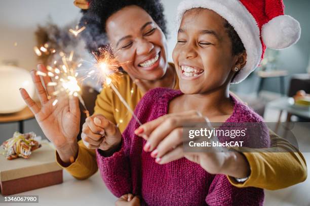 retrato de una madre y su hija sosteniendo bengalas de año nuevo en casa - christmas family fotografías e imágenes de stock