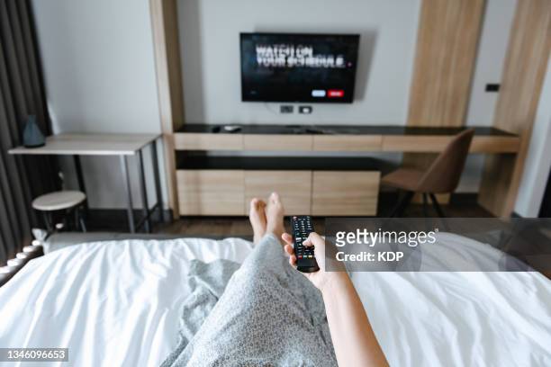 close-up of female hand is switching through television channels with remote control while relaxing in bedroom. - remote controlled 個照片及圖片檔