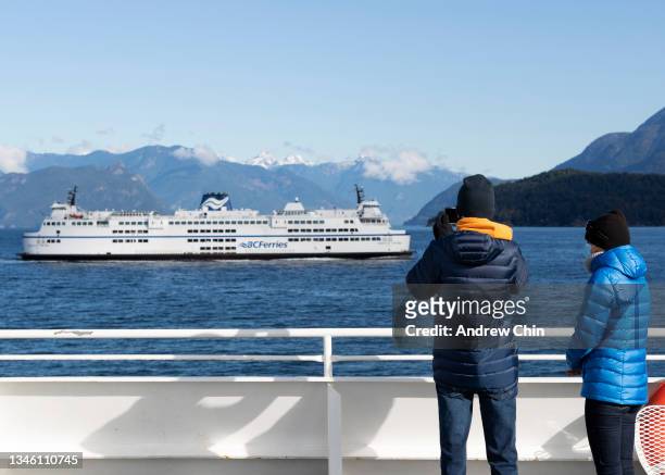 Man takes a picture of a ferry with a cell phone while a woman wearing a protective face mask looks on as they ride the ferry to Bowen Island during...