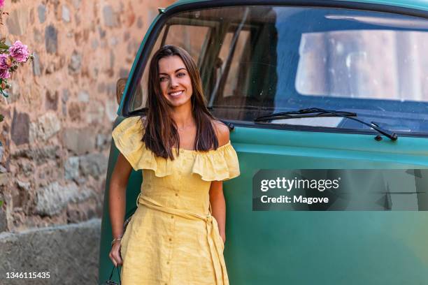 nahaufnahme einer schönen frau, die in die kamera lächelt, mit einem oldtimer im hintergrund. - hände in den taschen stock-fotos und bilder