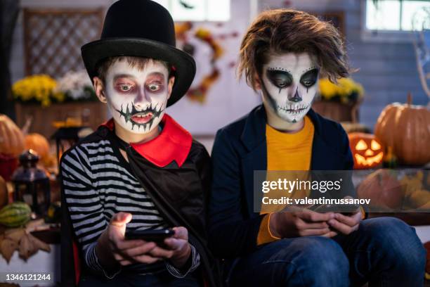 boys dressed in halloween costumes sitting on the stairs in front of the house and using smart phone trick or treat - pumpkins in a row stock pictures, royalty-free photos & images