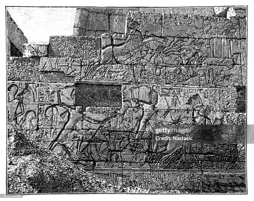 Close up section of a temple wall, covered in bas reliefs and carvings of battle scenes, with men in chariots, depicting the Poem of Pentaur, within the temple complex of Karnak