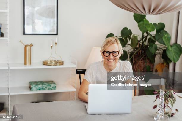 smiling woman using laptop at home - einzelne frau über 40 stock-fotos und bilder