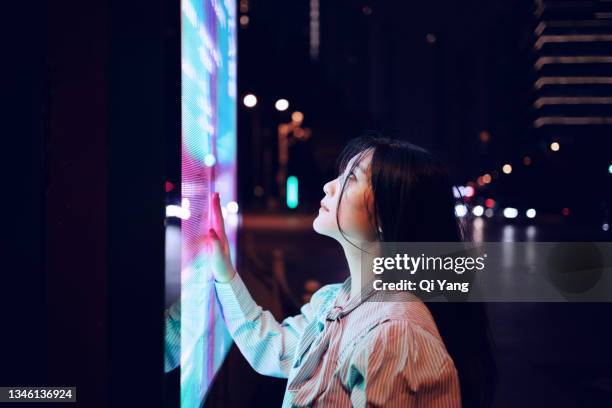 young woman using touch screen on the street in shanghai, china - billboard night stock-fotos und bilder