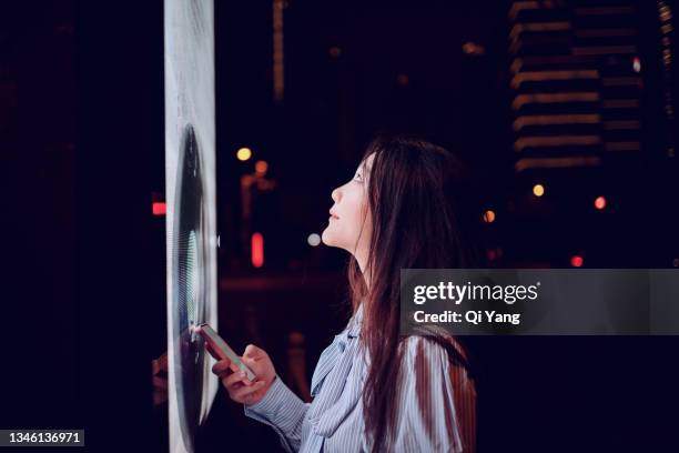 young woman using a smart phone connected to a touch screen in the street - angeleuchtet zahlen mensch stock-fotos und bilder