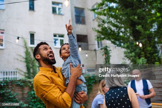 happy father holding his small son pointing to light bulb during family dinner outdoors in garden. - couple celebrating stock pictures, royalty-free photos & images