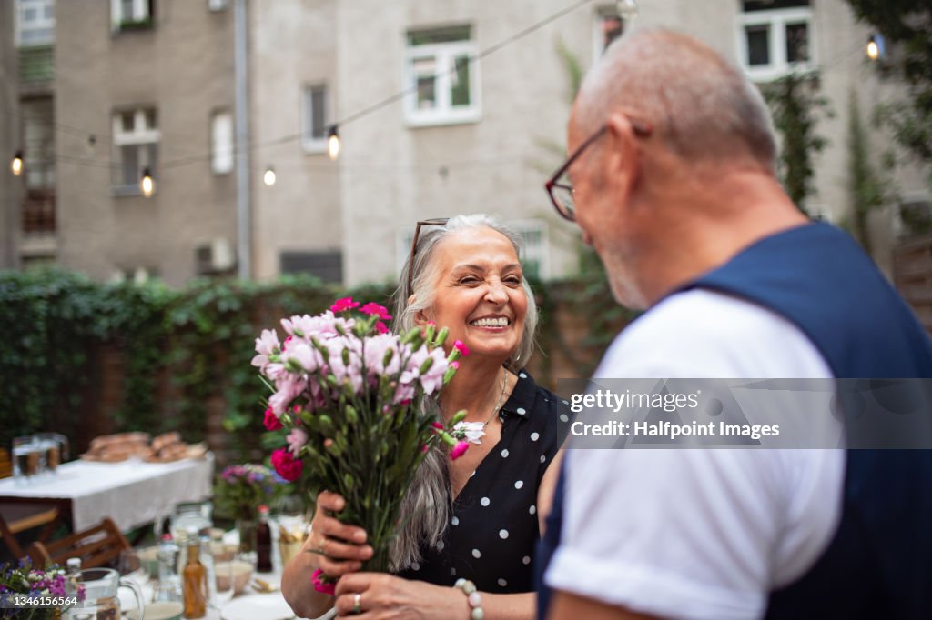 Happy senior woman getting bouquet from her husband outdoors in garden.