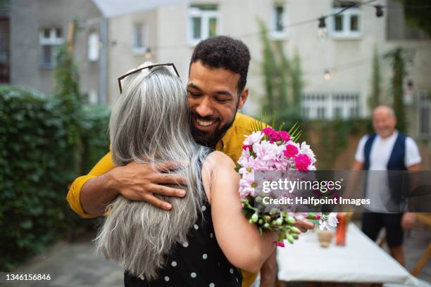 happy african american man with bouquet hugging his senior mother in law outdoors in garden. - man giving flowers foto e immagini stock