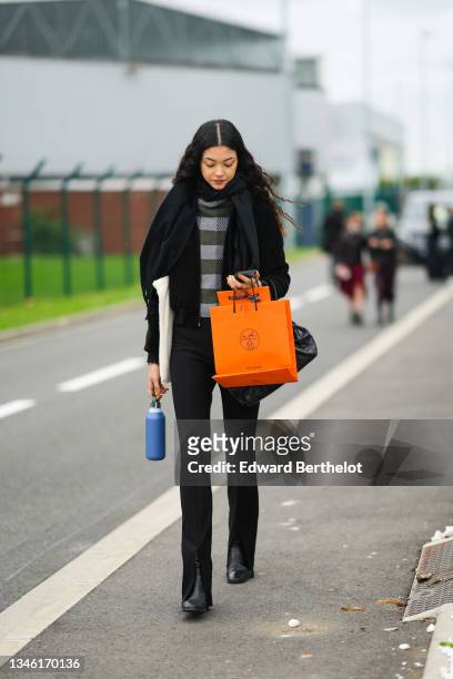 Guest wears a dark gray and dar green striped turtleneck pullover, a black wool pullover, a white latte shoulder bag cotton tote-bag, a black coat,...
