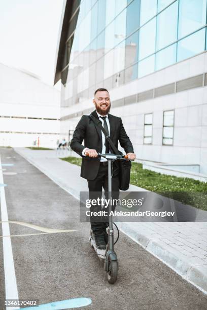 uomo d'affari barbuto sorridente che va al lavoro in scooter elettrico - smoking issues foto e immagini stock