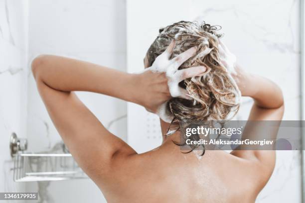 rear view of female taking shower and washing hair - haircare stockfoto's en -beelden