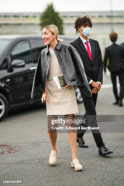 Guest wears a black shiny leather shirt jacket, a beige t-shirt, a beige leather high waist belted skirt, beige leather nailed / studded mules from...