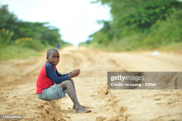 full length of boy sitting on dirt road,mozambique - mozambique stockfoto's en -beelden