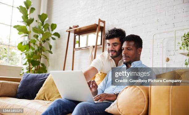 smiling young gay working on a laptop in their living room - homoseksuele man stockfoto's en -beelden