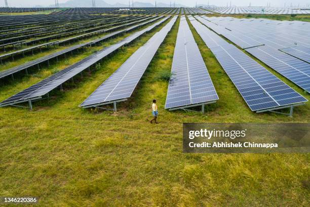 An aerial view shows a shepherd walk past photovoltaic cell solar panels in the Pavagada Solar Park on October 11, 2021 in Kyataganacharulu village,...