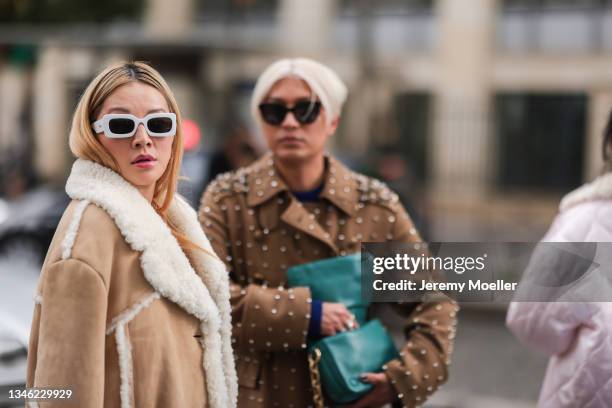 Tina Leung and Bryan Boy wearing a brown fur coat, white sunglasses and a brown bag and a brown coat with rivets and a green bag outside Miu Miu Show...