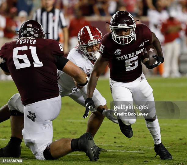 Devon Achane of the Texas A&M Aggies runs with the ball as he gets a block from Bryce Foster on Henry To'oTo'o of the Alabama Crimson Tide at Kyle...