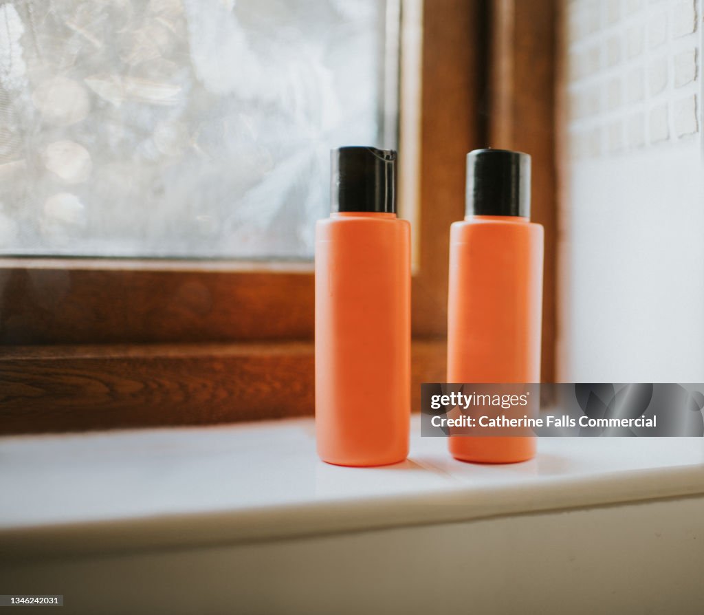 Two Shampoo bottles sitting on a tiled windowsill