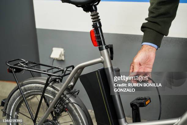 hand of caucasian man changing battery pack on electric bicycle at garage. transport concept. - ebike stockfoto's en -beelden