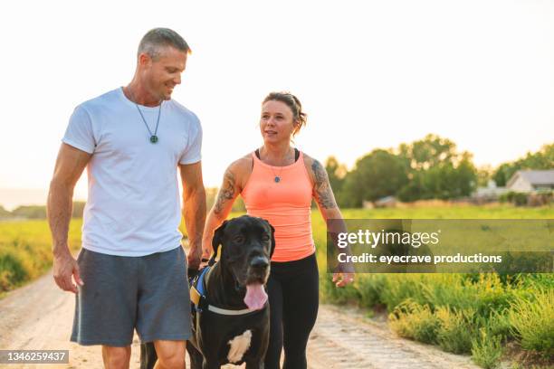 healthy fit body-builder couple walking and playing with black great dane dog in rural western usa at golden hour photo series - 40 49 years stock pictures, royalty-free photos & images