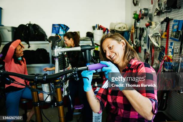 medium shot of smiling woman working on mountain bike in garage with friends - medium group of people foto e immagini stock