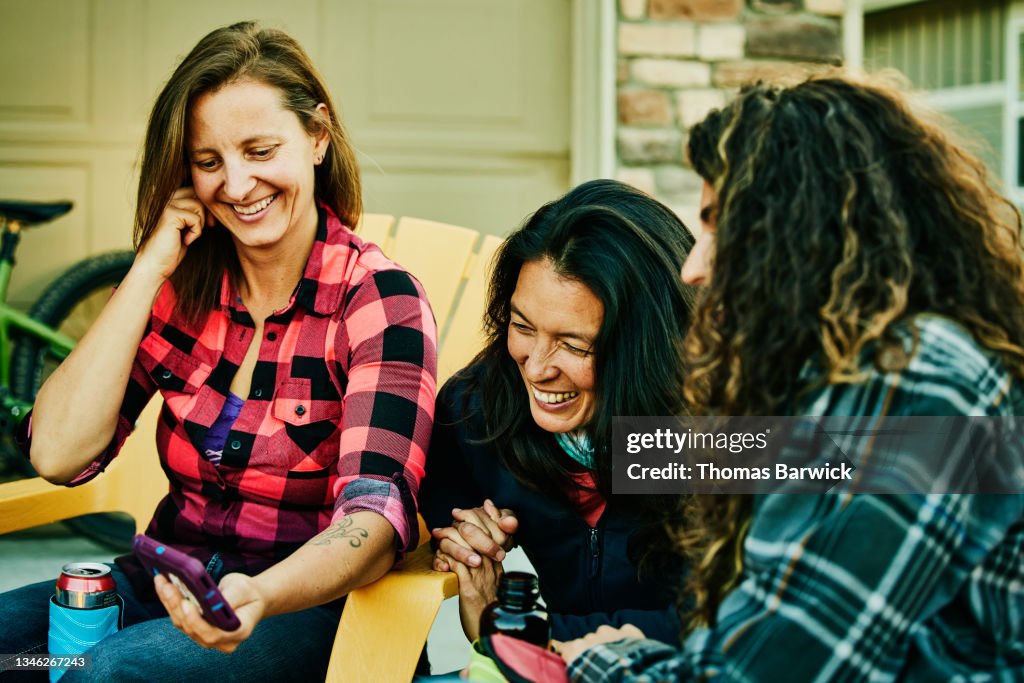 Medium shot of smiling female friends looking at video on smart phone while hanging out after mountain bike ride