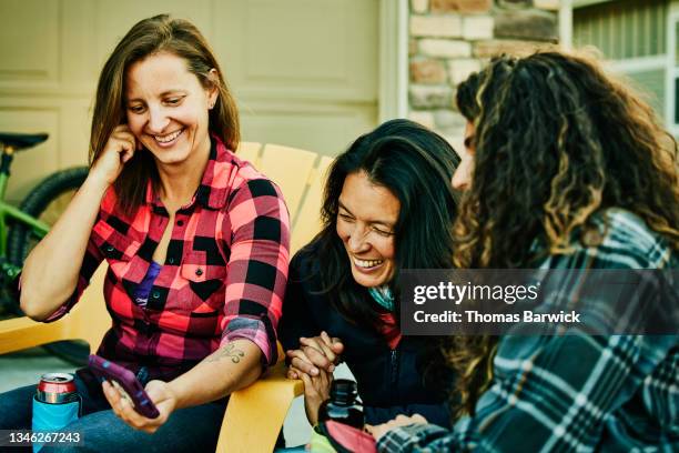 medium shot of smiling female friends looking at video on smart phone while hanging out after mountain bike ride - co op stock pictures, royalty-free photos & images