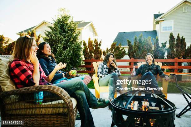 wide shot of smiling and laughing female friends hanging out by fire in backyard - buraco de fogueira imagens e fotografias de stock