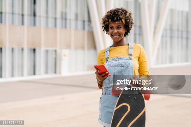 urban stylish skateboarder woman browsing on her mobile phone while standing outdoors. - woman longboard stock-fotos und bilder