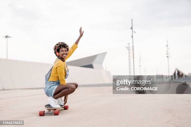 nice afro woman riding a skateboard and listening to music. - woman longboard stock-fotos und bilder