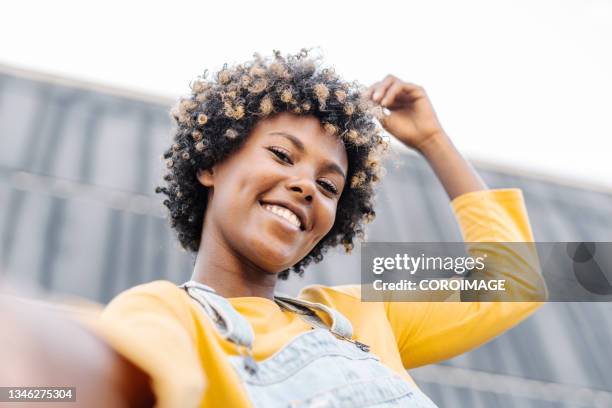 carefree afro woman with headphones looking at camera and smiling while taking a selfie outdoors. - selfie woman bildbanksfoton och bilder